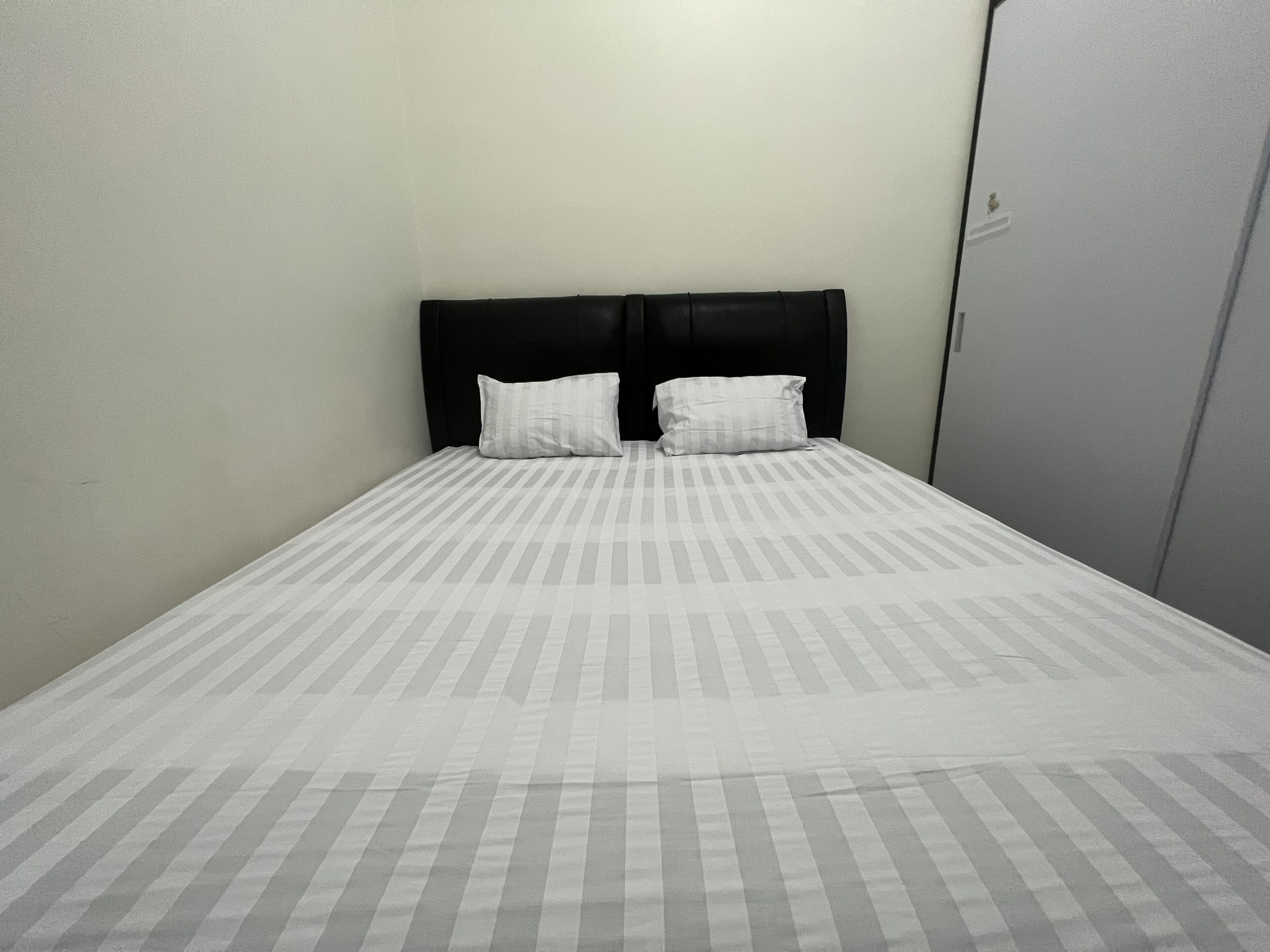 A single bed with a black headboard and two white pillows, a plain wall, and a door to the right.