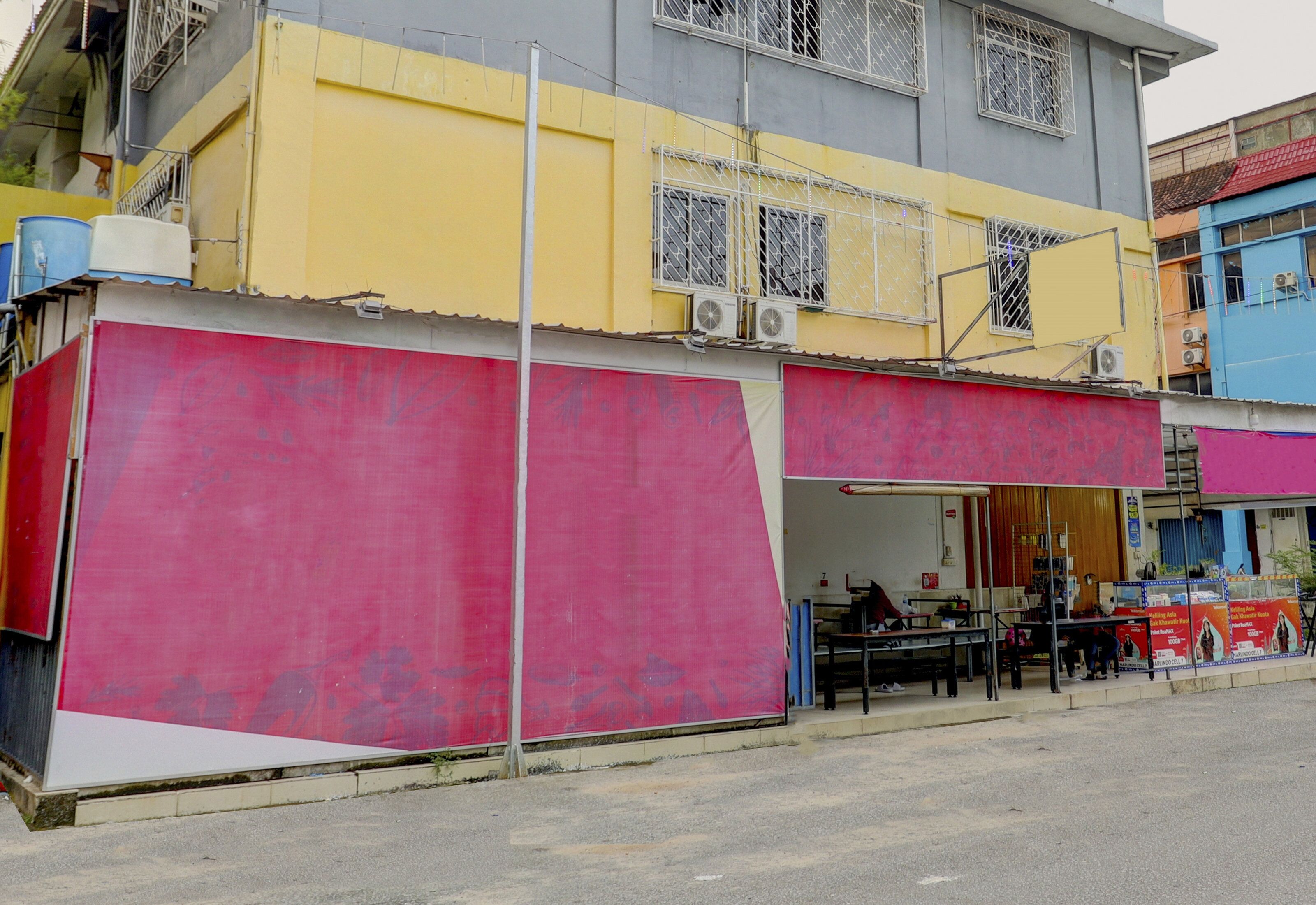 A multi-story building with a red storefront, air conditioning units, and a balcony with metal railings.