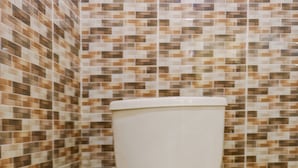 Un inodoro en un baño con paredes y suelo de baldosas decorativas.