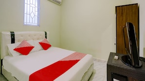 Habitación de hotel con cama, ventana, equipo de aire acondicionado, puerta de madera y televisor sobre una mesa.
