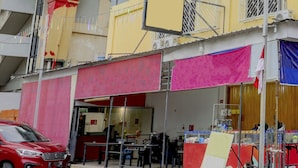 Un edificio con escaparate, un coche rojo estacionado delante y un extintor visible.