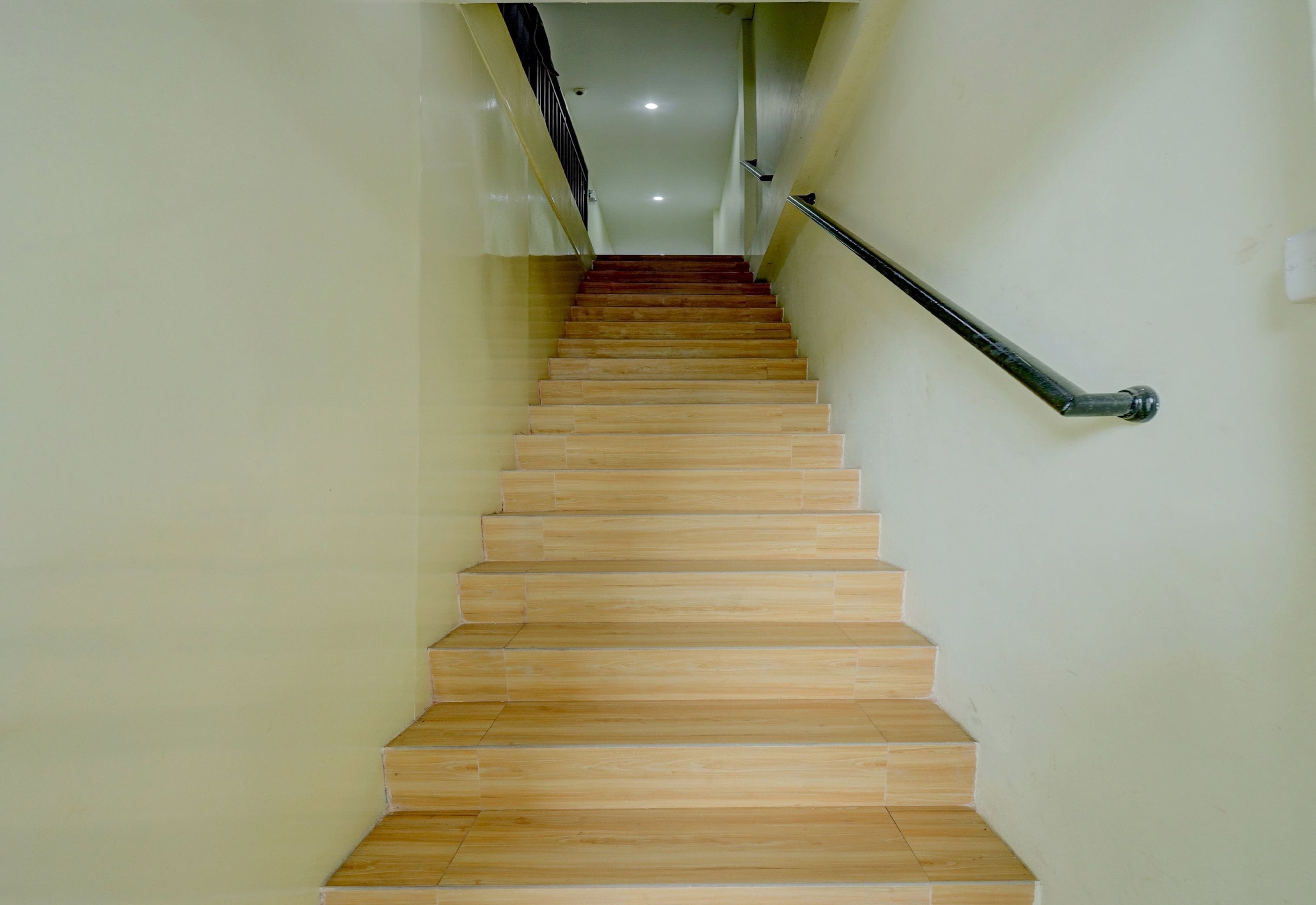 A wooden staircase with a handrail, leading to a landing with a ceiling light.