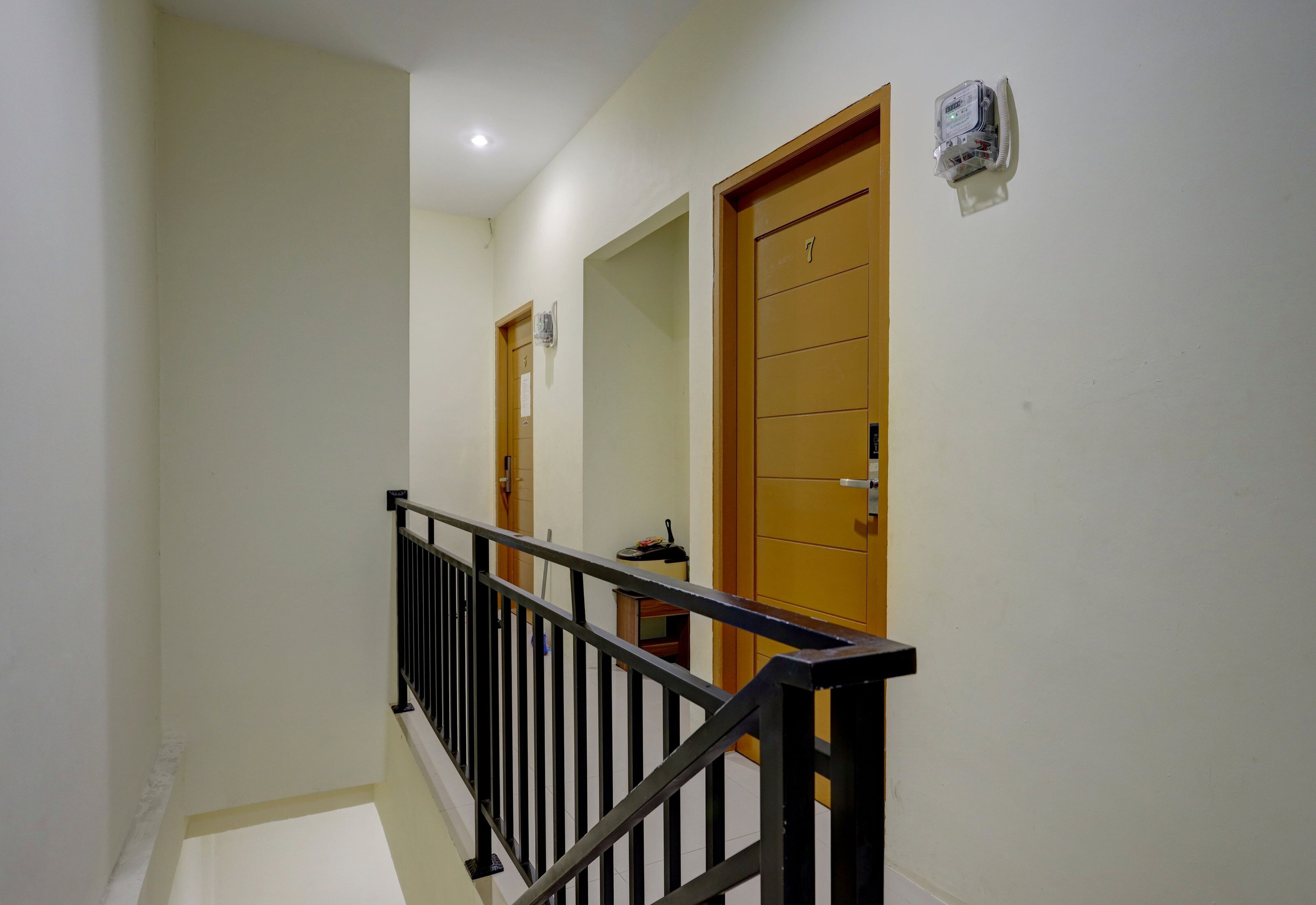 Um corredor com porta de madeira, corrimão de metal e luminária no teto.