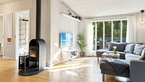 A modern living room with a fireplace, wooden flooring, a sofa, and a large window offering a view of the outdoors. - "Arwin" - 200m from the sea by Interhome (Hadsund)
