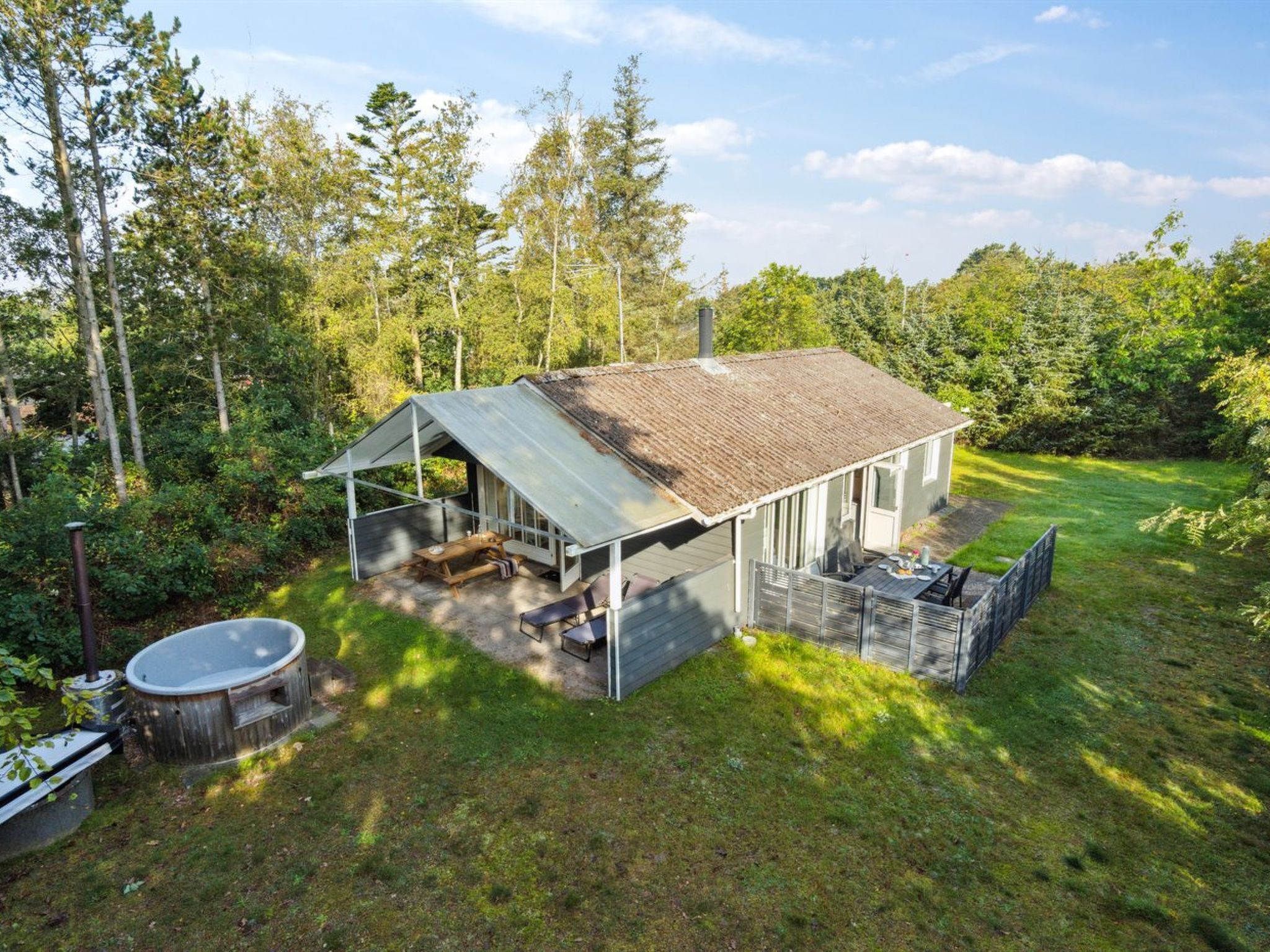 A small cabin with a metal roof, a covered patio, and a hot tub in a wooded area.