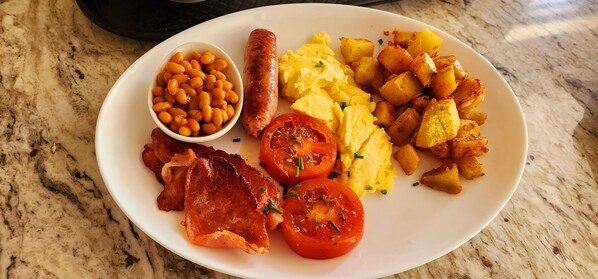 A plate of breakfast food including sausages, eggs, potatoes, beans, bacon, and tomatoes.