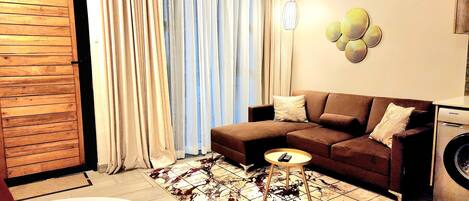 Un salon avec un canapé d’angle marron, une petite table ronde, un lave-linge et un tapis à motifs.