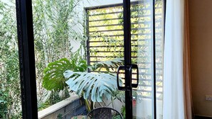 A modern room with large glass doors leading to a patio area with a table and chair, surrounded by pebbles and plants. - Instahomes by Tru - Garden Suites (Blantyre)