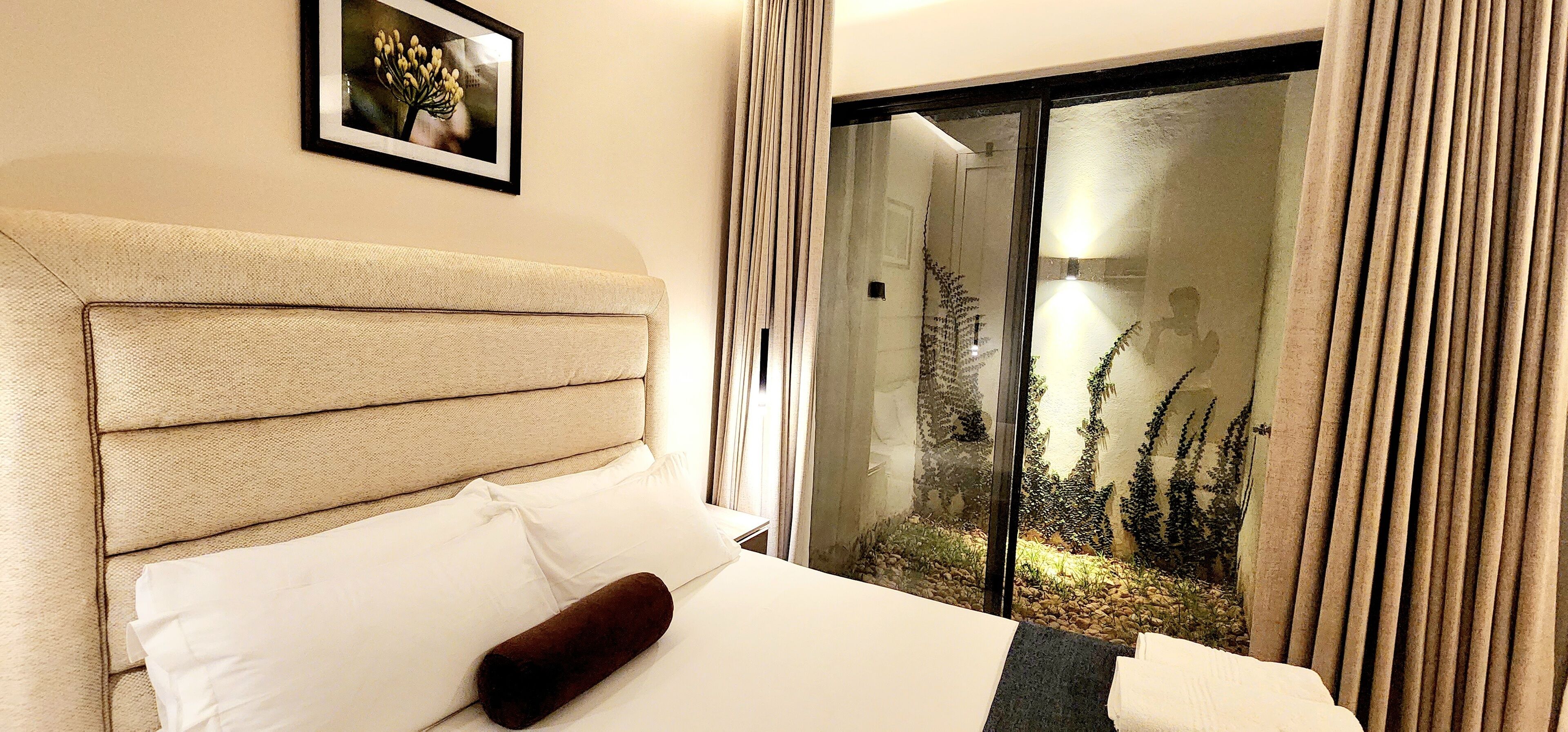 Habitación de hotel con cama, cabecero, ventana con cortinas y un cuadro en la pared.
