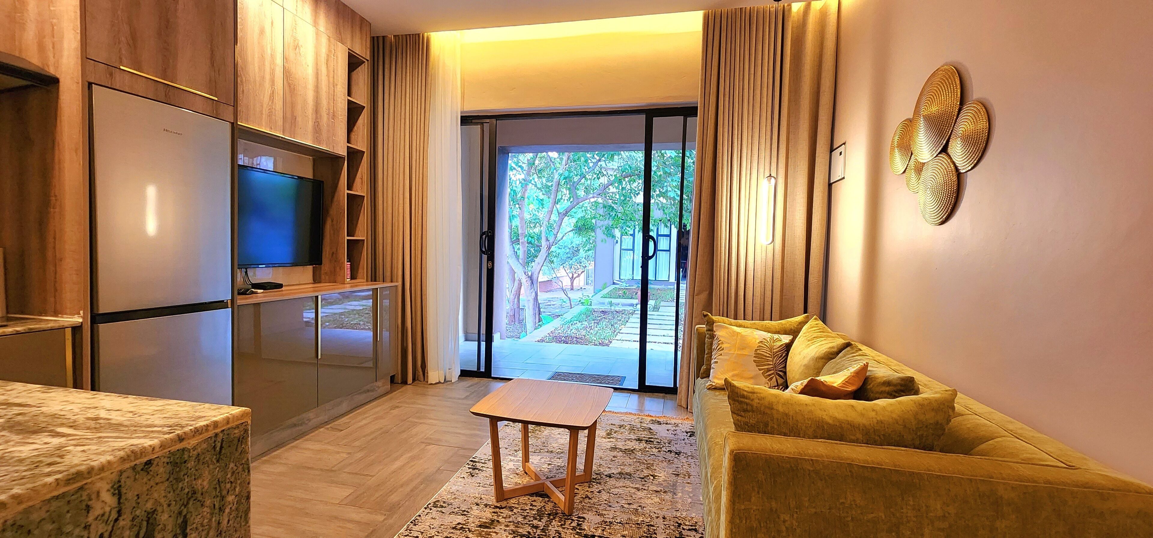 Una sala de estar moderna con sofá, una mesa de centro, un televisor de pantalla plana y una zona de cocina con armarios y un refrigerador.