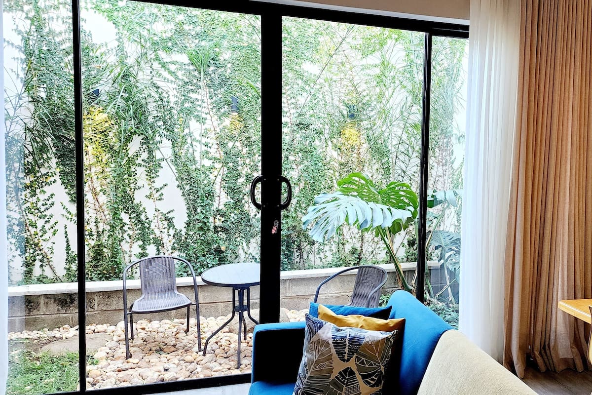 Un salon moderne doté d’une grande porte-fenêtre coulissante donnant sur un jardin, d’une table à manger en bois et d’un coin salon confortable avec un canapé et des fauteuils.