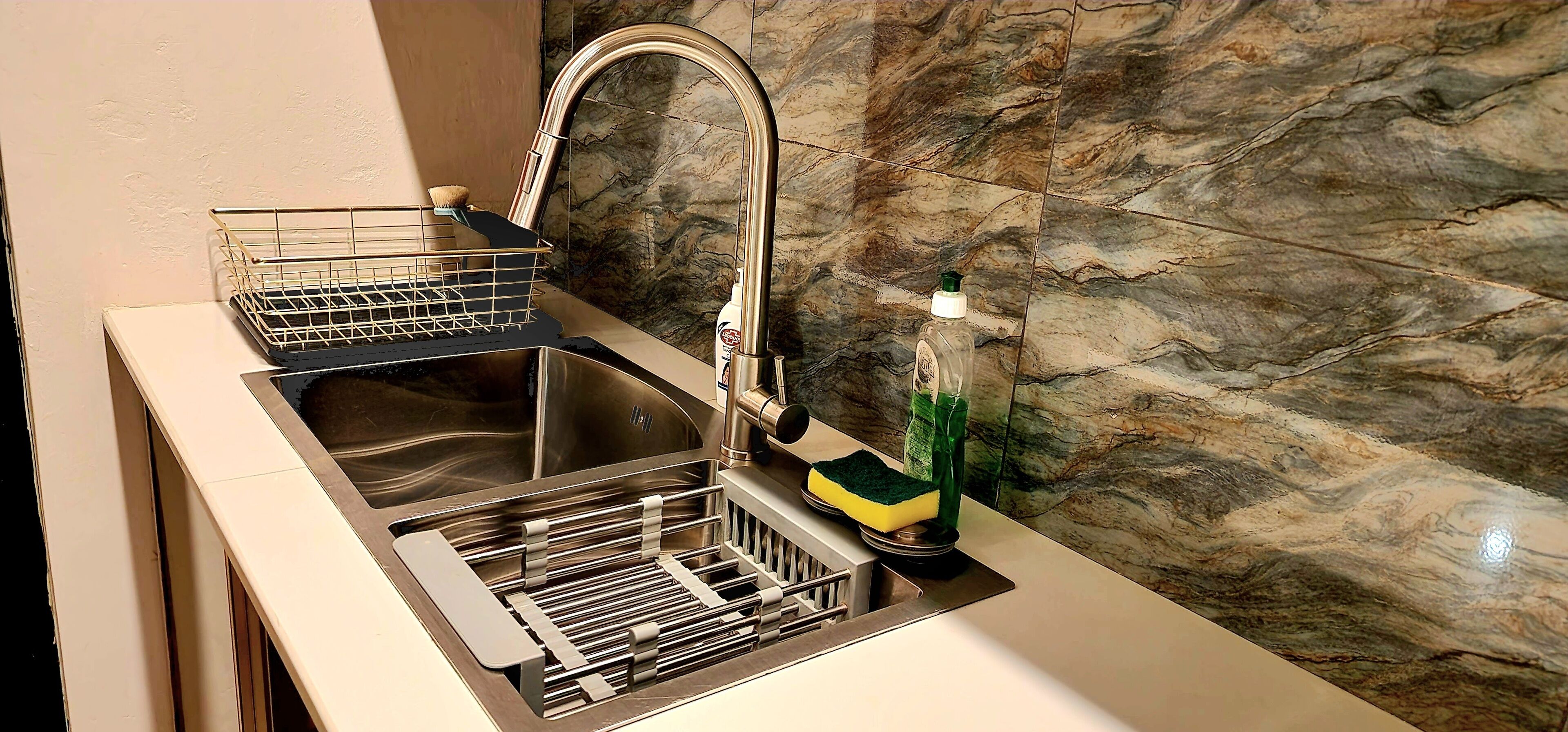 Una cocina con un lavamanos de acero inoxidable, un escurreplatos y una botella de detergente.