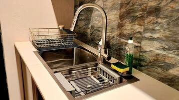 Una cocina con un lavamanos de acero inoxidable, un escurreplatos y una botella de detergente.