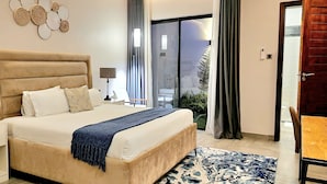 A bedroom with a large bed, bedside lamps, a nightstand, a patterned rug, and a view of the outdoors through a sliding door. - Instahomes by Tru - Garden Suites (Blantyre)