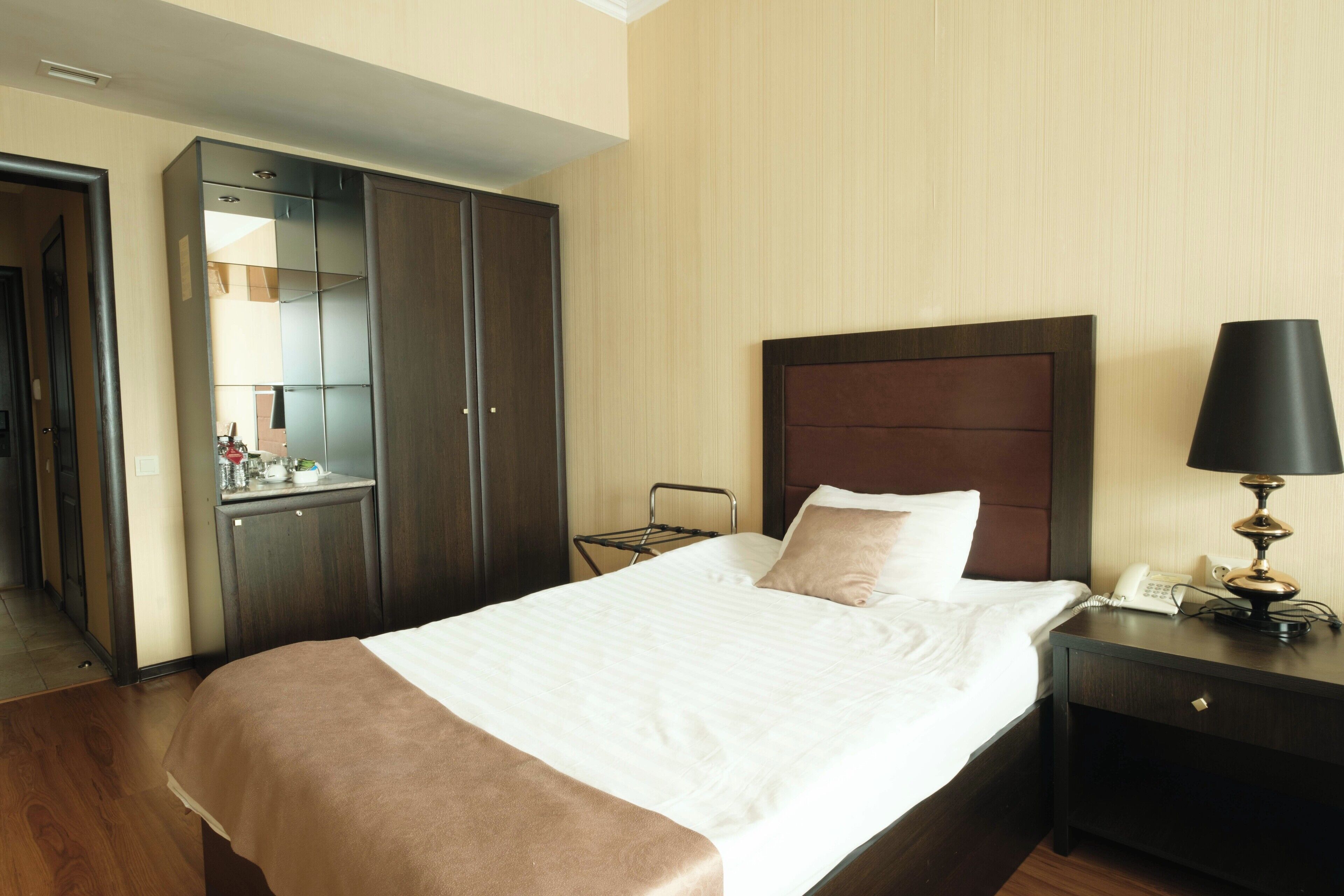 A hotel room with a large bed, a wardrobe, a bedside table with a lamp, and a telephone.