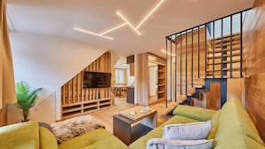 Una sala de estar moderna con un sofá verde, un televisor y una escalera con barandillas de madera.