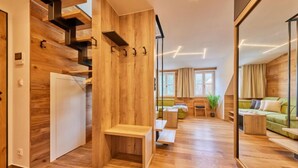 Un interior moderno con suelo de madera, una escalera, una zona de estar con sofá y una mesa, y un espejo grande que refleja la habitación.