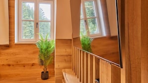 Un interior de madera con una escalera, una planta en maceta y un ventanal con vistas a árboles.