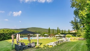 Un jardin avec une piscine, des chaises longues et un kiosque.