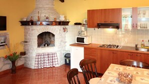 A kitchen with a stone fireplace, wooden cabinets, a microwave, and a dining table with chairs. - Vacation home Milena by Interhome (Barban)