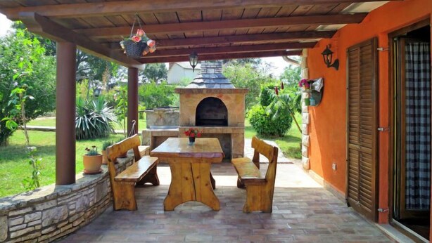 An outdoor patio with a stone oven, wooden benches, and a covered area with a pergola. - Vacation home Milena by Interhome (Barban)