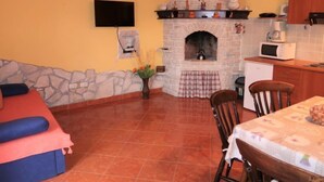 A cozy kitchen with a stone fireplace, a television, and a dining area with a table and chairs. - Vacation home Milena by Interhome (Barban)