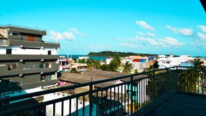 A multi-story building with balconies, a view of the sea, and a distant hill with buildings. - Catamaran 6 Guest Inn (Trincomalee)