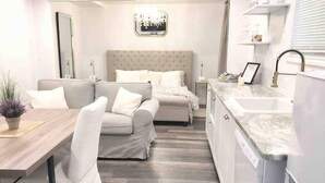 A modern, well-lit bedroom with a large bed, a sofa, and a dining area. - Romantic Couples Getaway - Sauna, Hot Tub, Private Beach access, Hiking trails (Lambton Shores)