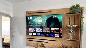 Een aan de muur bevestigde televisie met houten lijst, omringd door planken met decoratieve objecten en een mand.