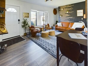 A modern living room with a brown leather sofa, a dining table with chairs, a patterned rug, and a wall-mounted plant arrangement. - 🌿  Modern Earthy Bungalow | KING Beds • A/C • Pet-Friendly Fenced Yard (Corvallis)