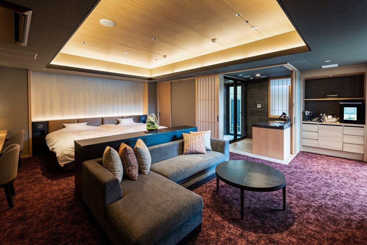 Een moderne hotelkamer met een bed, een bank en een salontafel. Het heeft een kitchenette en een schuifdeur naar buiten.