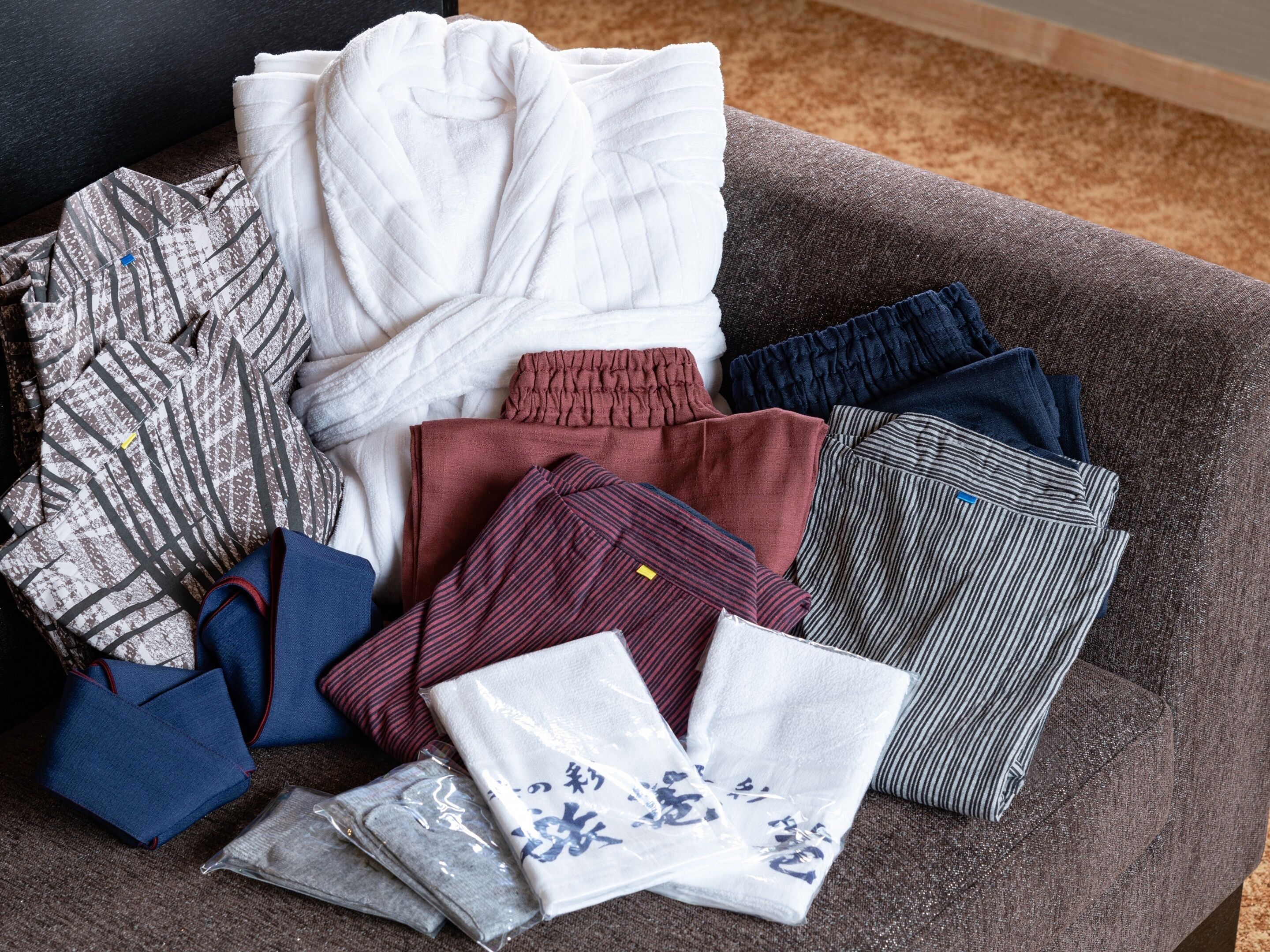A variety of neatly folded clothing items on a gray couch.