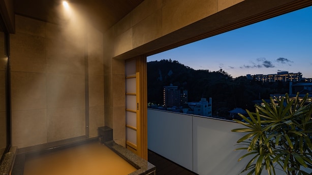 Un espace de baignade dans une source thermale, offrant une vue sur le paysage urbain au crépuscule.
