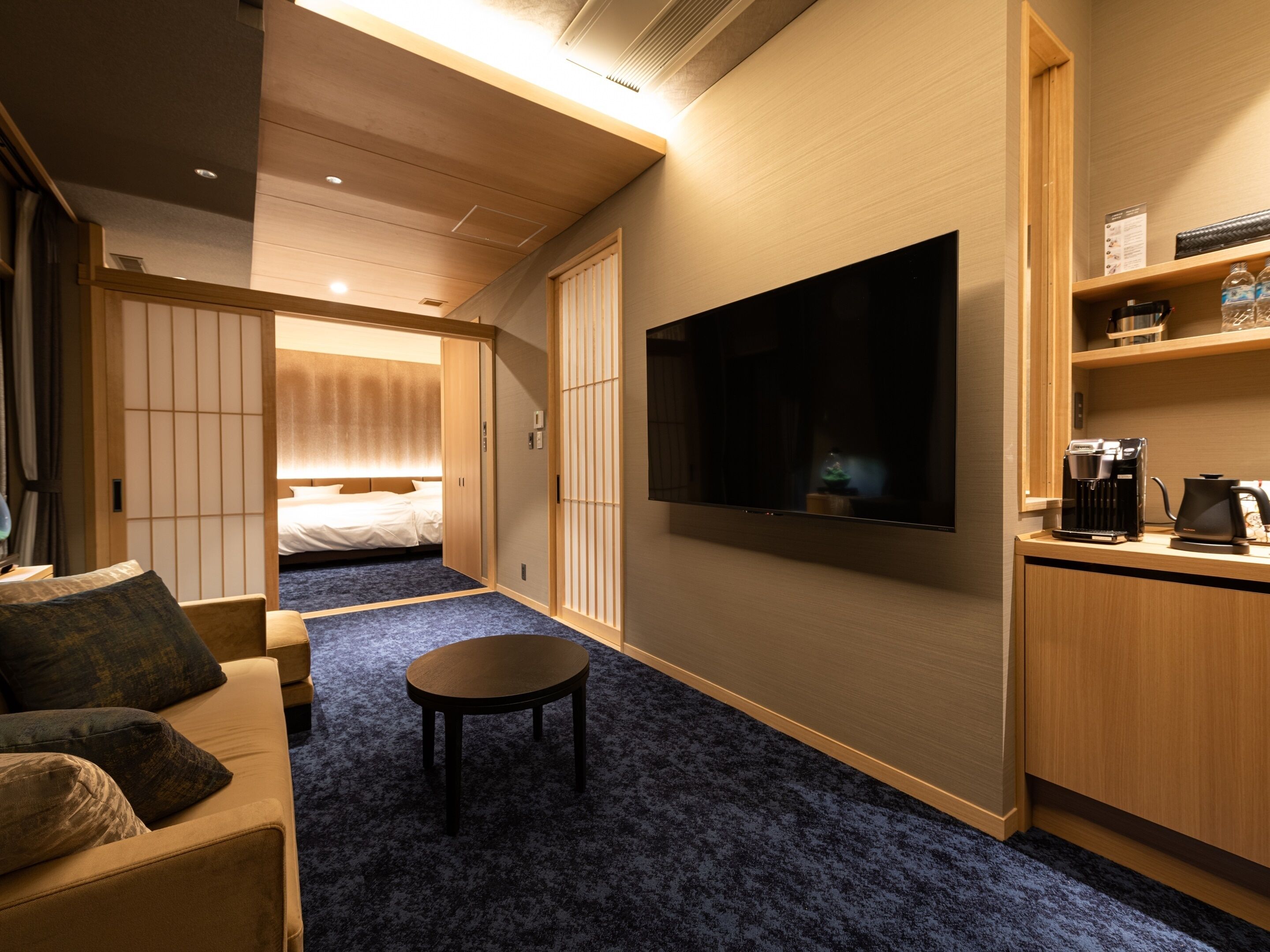 A hotel room with a bed, a TV, a coffee machine, and a small table.