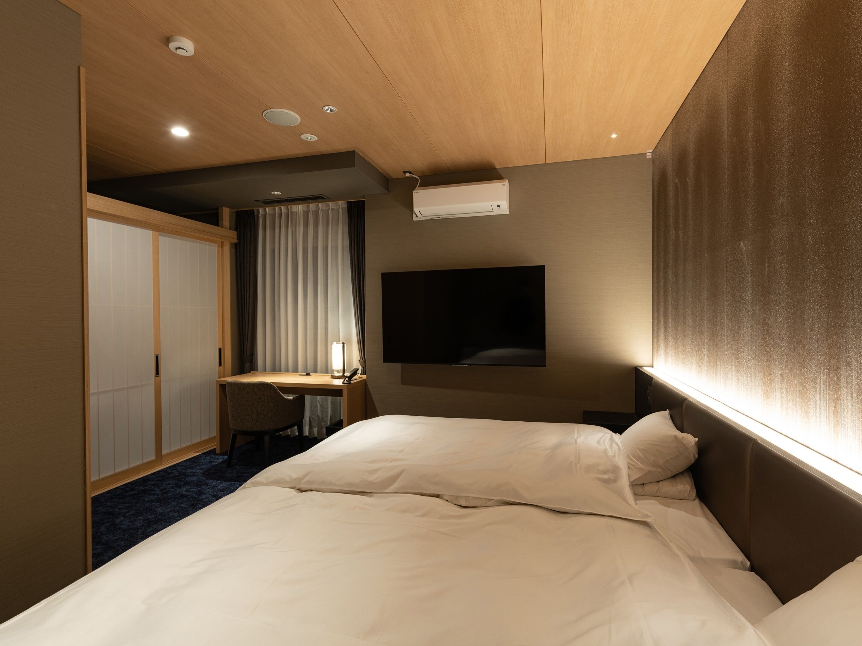 A hotel room with a bed, a desk, a chair, a television, and a wardrobe.