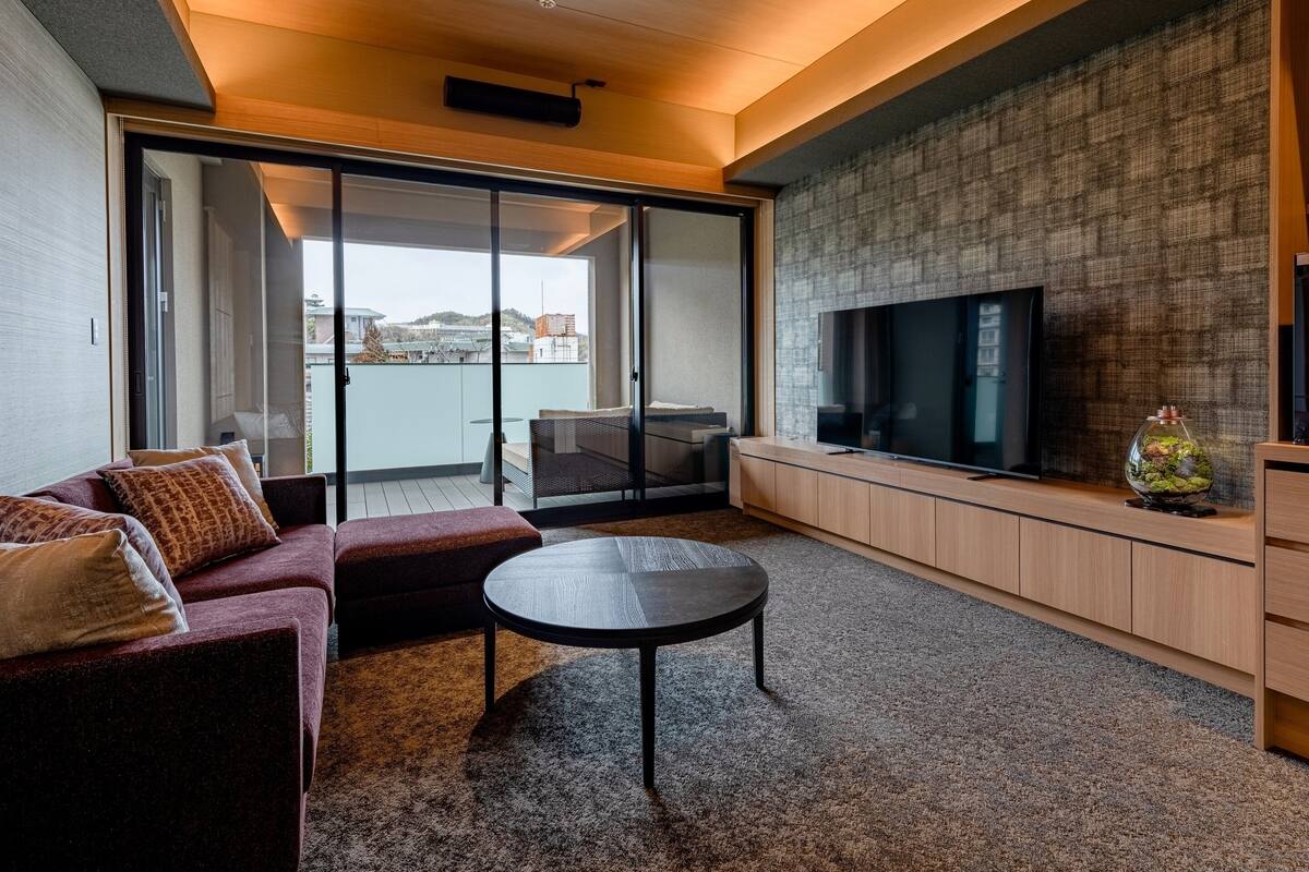 Een moderne woonkamer met een bank, een ronde salontafel, een televisie en een open haard.