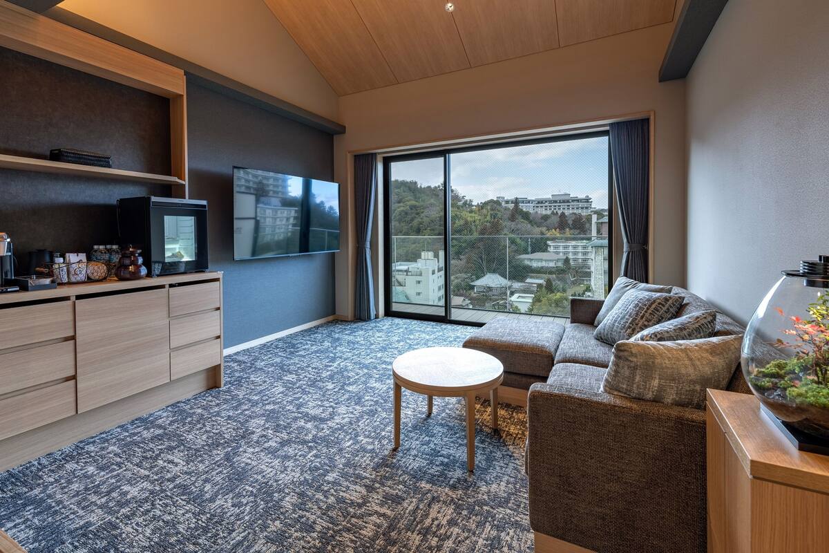Een moderne woonkamer met een bank, een salontafel, een televisie en een uitzicht op de stad door grote ramen.