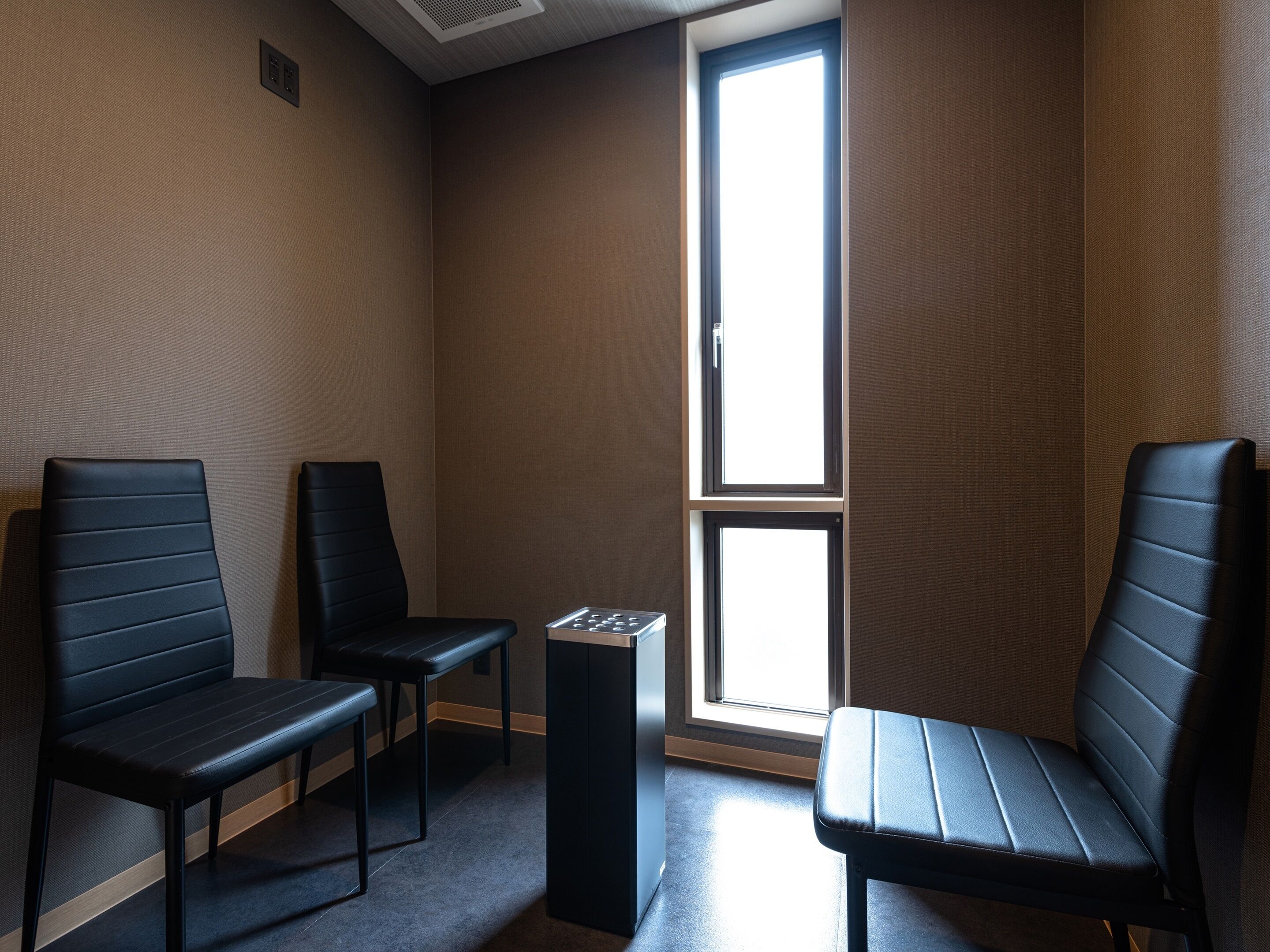 Una habitación con dos sillas negras, una mesita y una ventana.