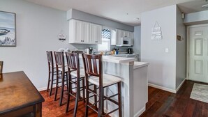 A compact kitchen with white cabinets, a central island, and a dining area with wooden chairs. - Tranquil 2-Bedroom Pointe Royale Condo (Branson)