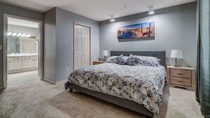 A bedroom with a bed, bedside tables, a nightstand, a door, and a painting on the wall. - Tranquil 2-Bedroom Pointe Royale Condo (Branson)