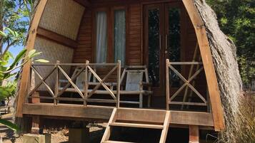 A wooden cabin with a thatched roof, a balcony with railings, and a ladder leading to the entrance.