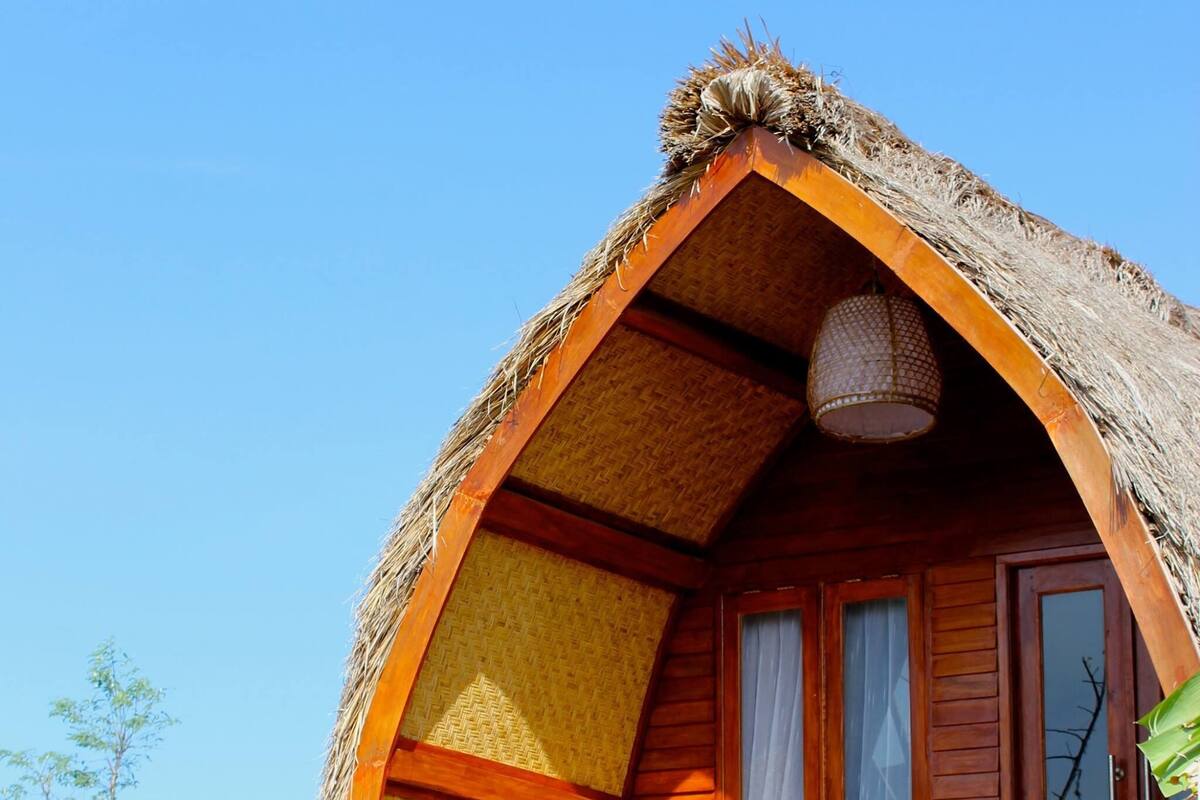 A thatched-roof cabin with a wooden balcony and a single window.