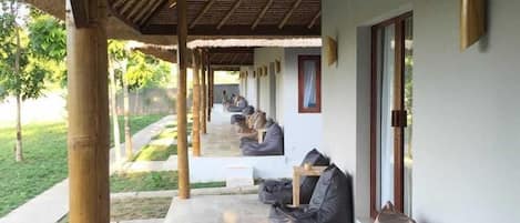 A covered outdoor seating area with bean bags and tables, bamboo pillars, and a view of the greenery.