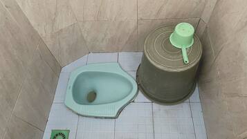 A small, tiled bathroom with a toilet and a green urinal.