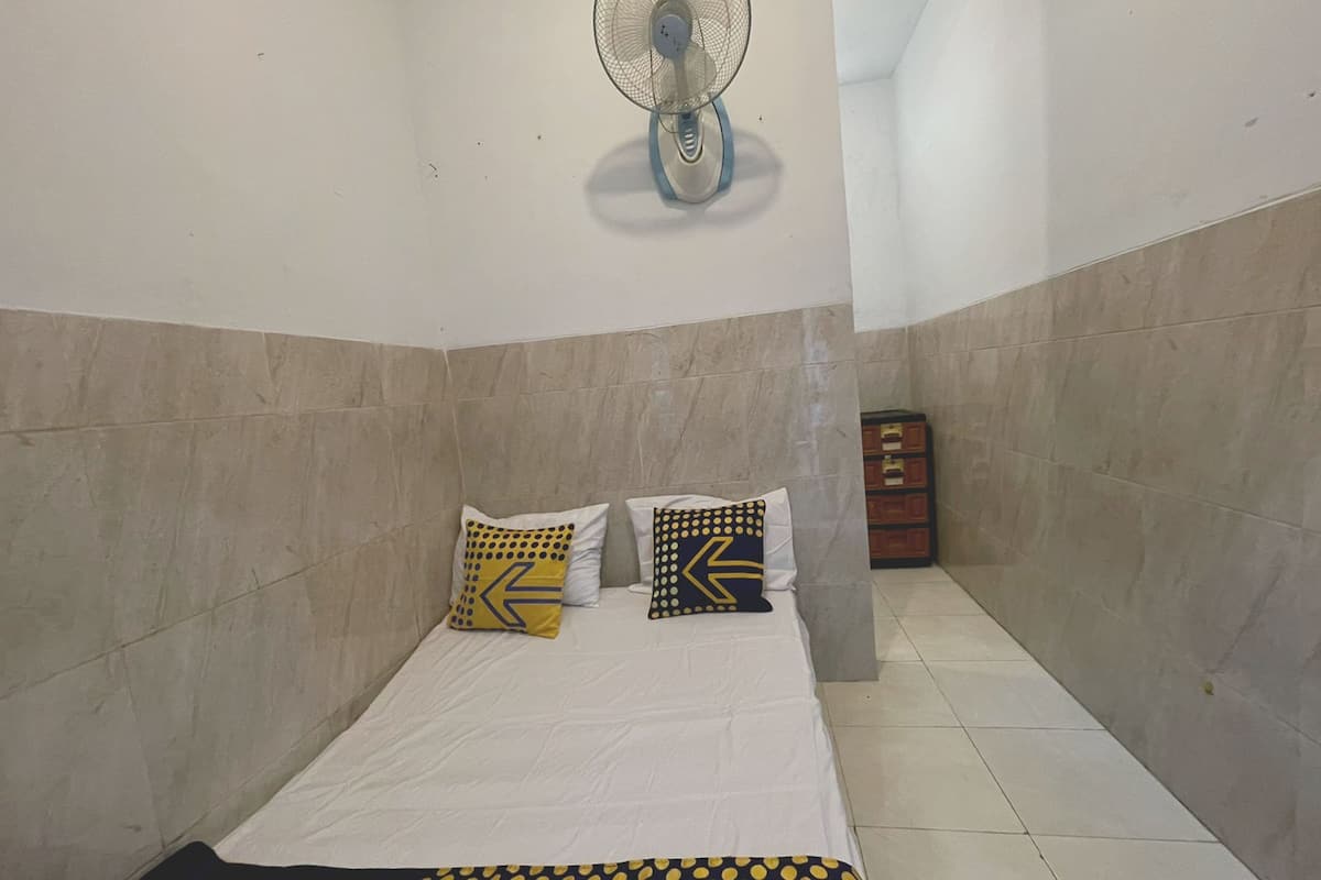 Una habitación pequeña y limpia con cama, ventilador de pared y armario.