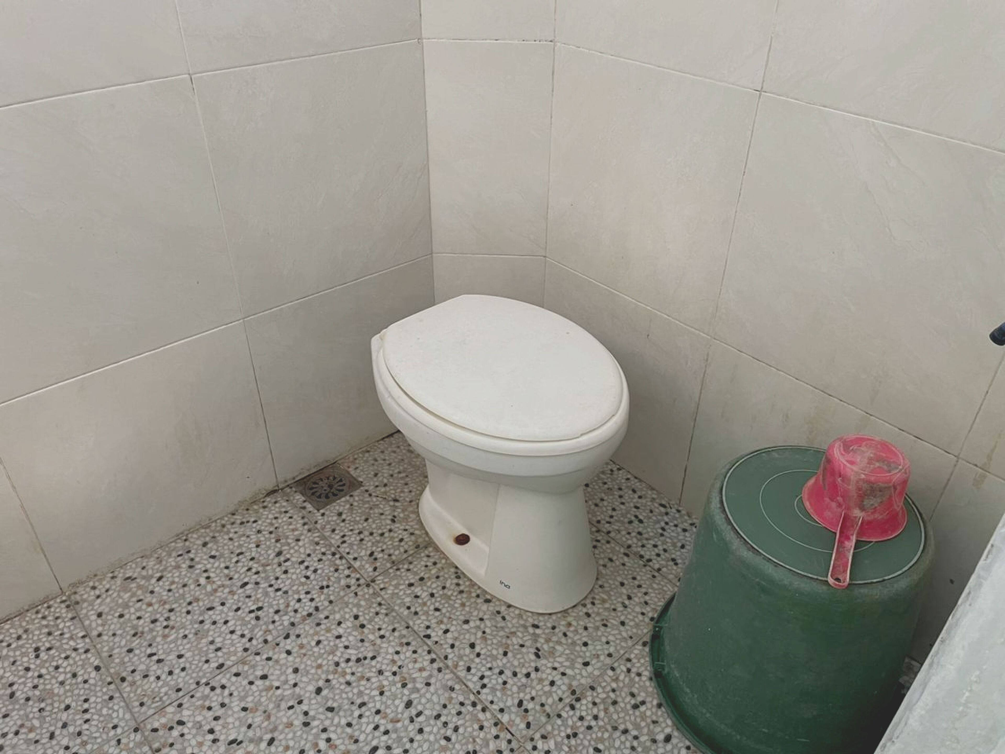 A small, clean bathroom with a white toilet, a green trash bin, and a speckled tile floor.