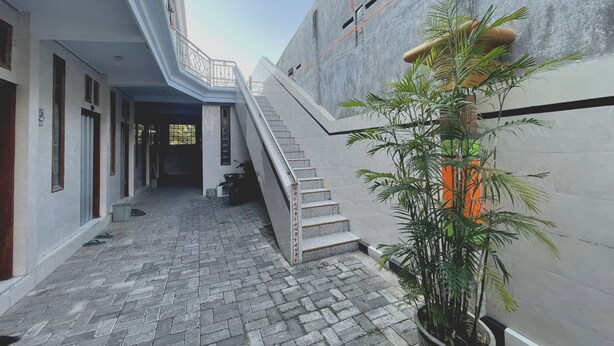 A building with a staircase leading to an upper level, a paved courtyard, and a potted plant. - Hotel O Karman's Sari Homestay Syariah (Gresik)