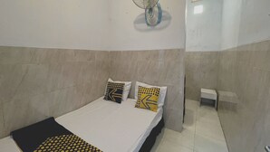 A bedroom with a bed, two pillows, a wall-mounted fan, and a small bedside table. - Hotel O Karman's Sari Homestay Syariah (Gresik)