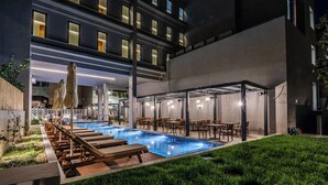 A modern hotel with a rooftop pool, outdoor seating, and a well-lit terrace.