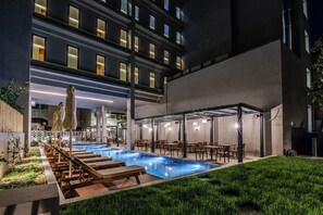A modern hotel with a rooftop pool, outdoor seating, and a well-lit terrace.